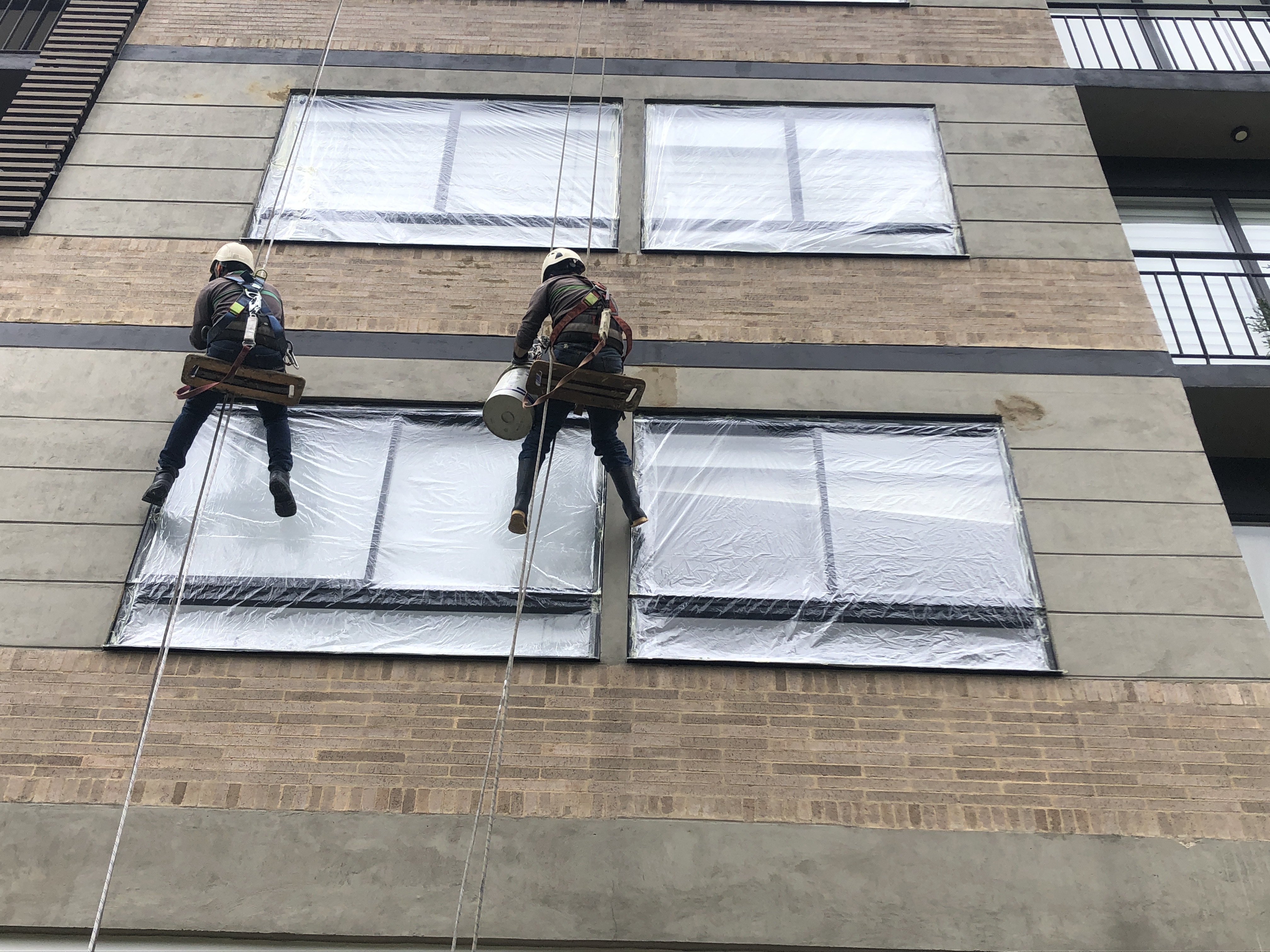 Dos trabajadores de alturas realizando el emboquillado del edificio luego del prelavado con agua a presión