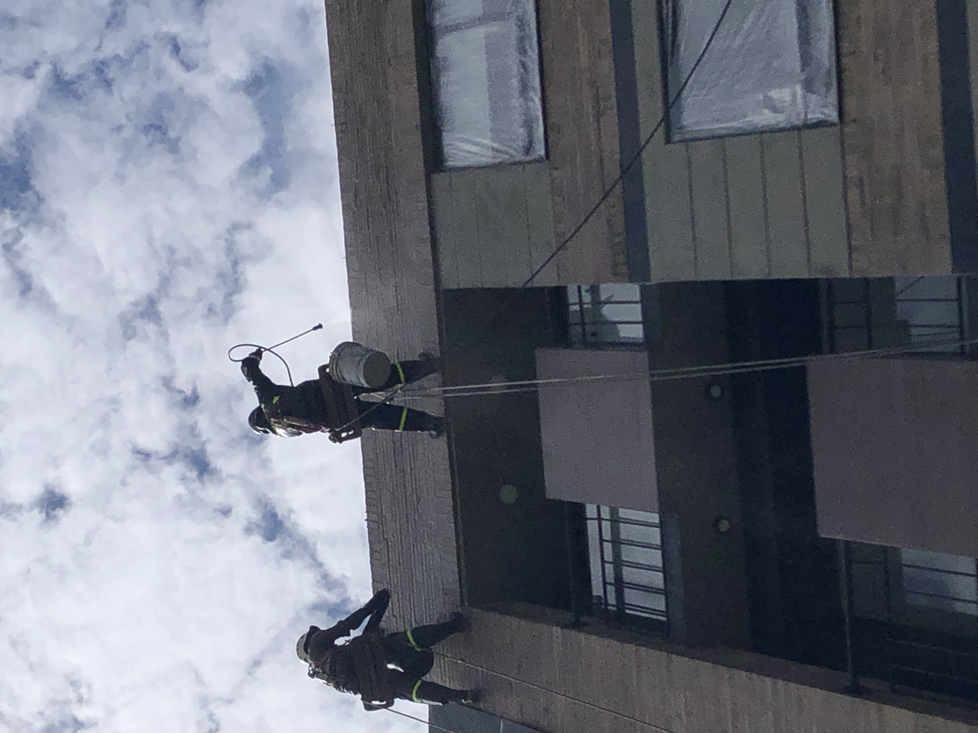 Dos trabajadores de alturas realizando el prelavado del edificio con agua a presión y desengrasante